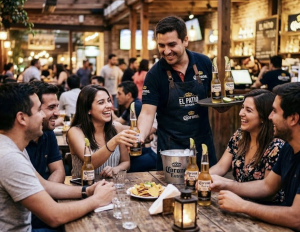 A group of friends cheers with Corona bottles at a rustic bar, smiles and laughter around a wooden table as a waiter serves drinks.